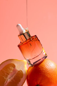 An elegant serum bottle rests on fresh oranges against soft pink
