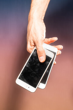 Hand gripping two broken smartphones