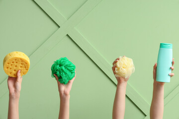 Female hands with bottle of cosmetic product and bath sponges on green background