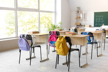 Interior of light classroom with desks, backpacks on chairs and blackboard