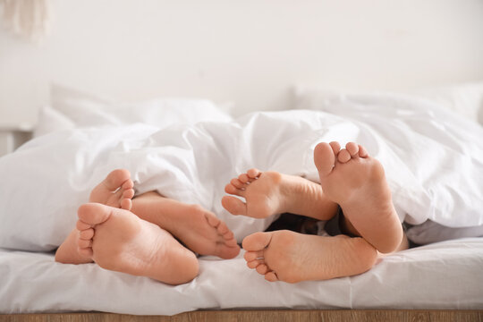 Feet of young man with two women lying under blanket in bedroom, closeup. Polyamory concept