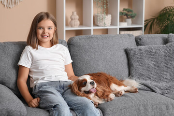 Cute little girl with King Charles spaniel dog sitting on sofa at home