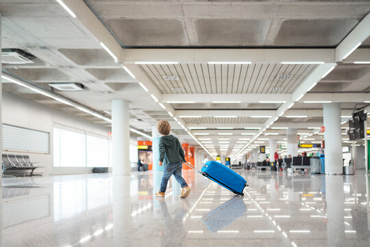 Little boy pulling suitcase walking in airport terminal