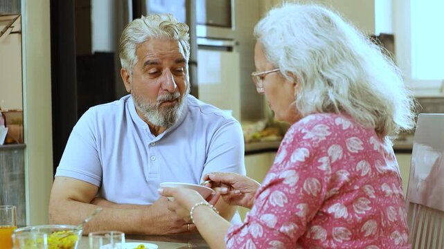 Happy retired senior indian couple eating healthy breakfast together, Romantic elderly husband wife sharing food at table, Love and bonding. Retirement life.