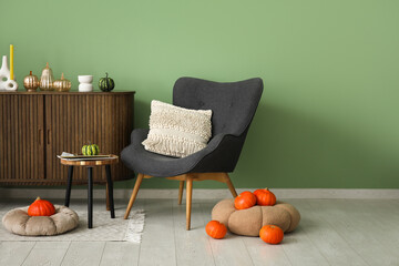 Comfortable armchair, coffee table, pumpkins and wooden chest of drawers in interior of living room