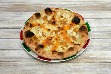 A pizza with cheese and chicken on it. The crust is brown and the cheese is yellow. The pizza is on a white plate