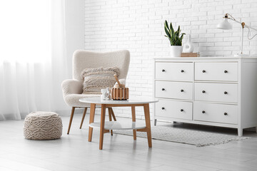 Interior of light living room with armchair, coffee table and chest of drawers