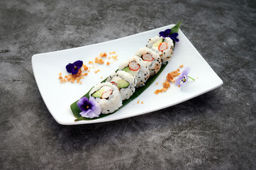 A plate of sushi with a purple flower on it. The plate is on a table