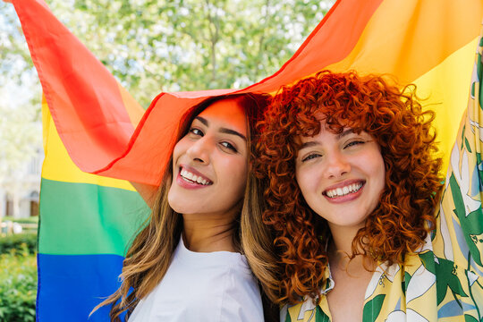 Diverse women embracing rainbow flag, symbolizing unity, love, and pride within lgbtq+ community during festive celebration