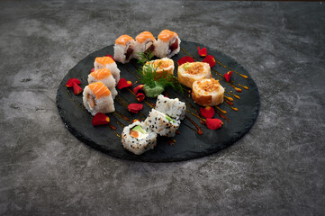 A plate of sushi with a variety of rolls and a sauce. The sushi is served on a black plate