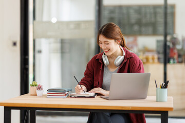 Young asian happy smiling Hispanic Asian student wearing headphones talking on online chat meeting using laptop in university campus or at virtual office. College female student learning remotely.
