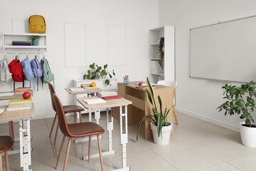 Interior of empty classroom with school desks, backpacks hanging on hooks and clean whiteboard