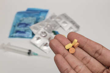 Close-up of a hand holding various pills and tablets with blurred medical supplies in the background