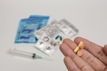 Close-up of a hand holding various pills and tablets with blurred medical supplies in the background