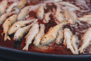 cooking fish in large round frying pan outdoors, fried smelt, close-up view, street food concept