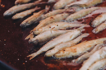 cooking fish in large round frying pan outdoors, fried smelt, close-up view, street food concept