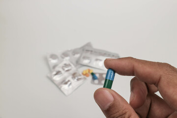 Close-up of a hand holding a single tablet with blurred medical supplies in the background
