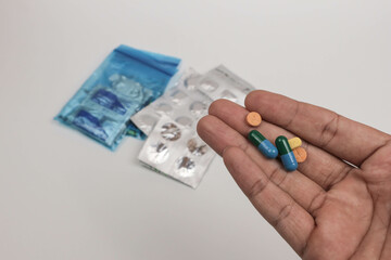 Close-up of a hand holding various pills and tablets with blurred medical supplies in the background