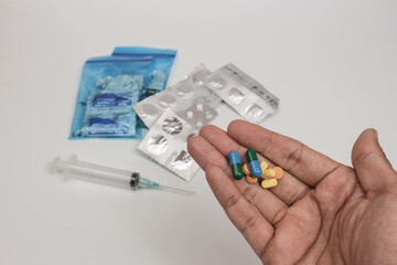 Close-up of a hand holding various pills and tablets with blurred medical supplies in the background