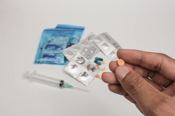 Close-up of a hand holding a single tablet with blurred medical supplies in the background