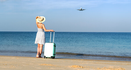 A woman with a suitcase on the beach meets a plane
