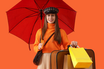 Female tourist in autumn clothes with umbrella and bags on orange background