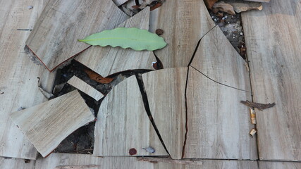 Damaged outdoor tile floor with cracks, scattered leaves and rough surface texture.