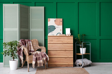 Stylish interior of living room with armchair, chest of drawers and folding screen