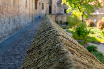 Historic stone wall guiding the viewer's gaze toward a vibrant garden pathway in a charming medieval village