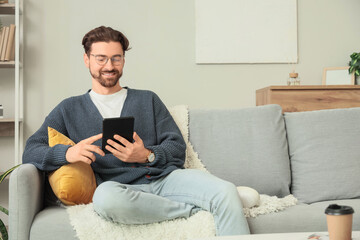 Young man with e-reader sitting on sofa at home