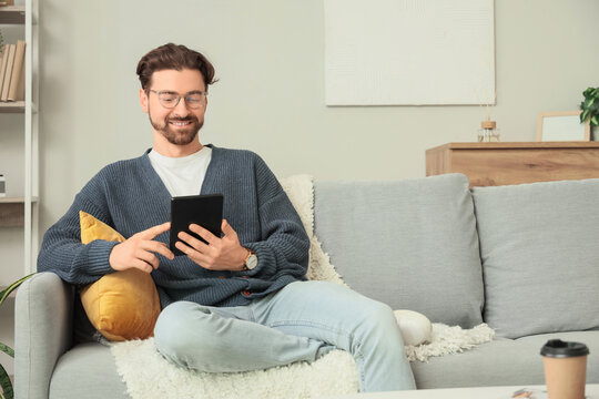 Young man with e-reader sitting on sofa at home