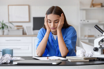 Tired female medical intern studying at table in clinic