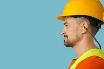 Male builder with earplugs on blue background, closeup