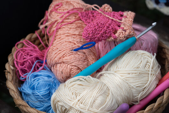Colorful yarn balls and crochet hooks resting in wicker basket