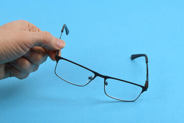 Hand holding plastic black glasses, isolated on blue background.