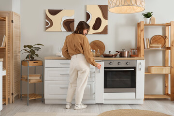 Young woman opening drawer in modern kitchen, back view