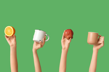 Female hands with orange, apple and mugs of tasty mulled wine on green background