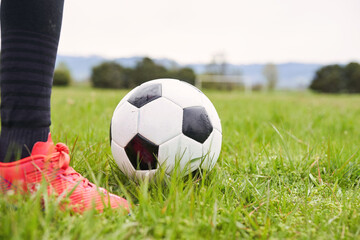 Closeup of soccer ball on grassy field next to player in red shoes