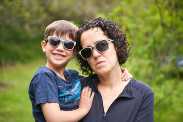 mother and young son posing with sunglasses in a greenery scenery