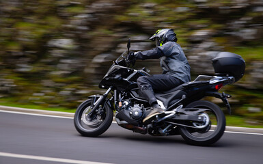 Fototapeta premium Driver riding motorcycle on empty asphalt road, blurred motiion, spring mountains