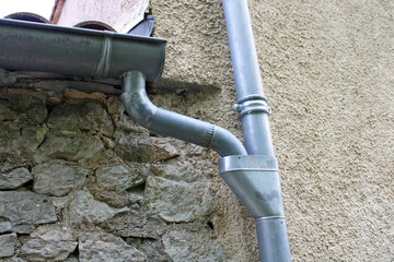 Gouttière en zinc gris et cuvette de branchement sur la façade de la maison en pierre
