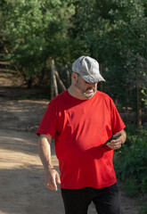 Naklejka premium Middle-aged man walking while using smartphone in the park