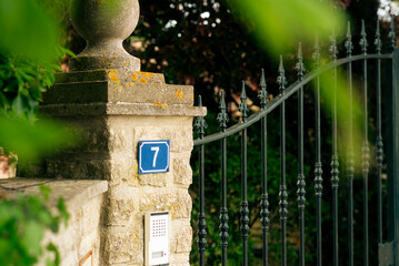 Ornate iron gate and stone pillar with number seven plaque in lush garden setting