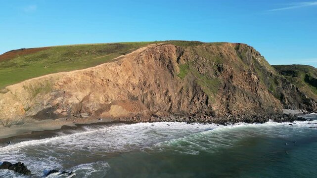 Drone view of Duckpool Beach rocky cliffs and calm blue sea, bathed in sunlight under a clear sky