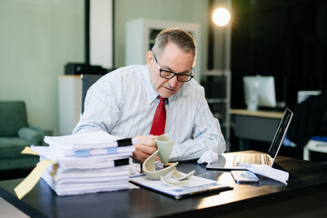 Obraz premium Angry and irritated Mature Businessman sitting in the office of laptop with his keyboard tired from work. Overwork, stress