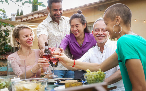 Cheerful mature friends toasting wine glasses, enjoying food and drinks at backyard summer dinner party