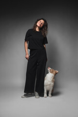 Young beautiful woman with curly hair and in black clothes with a border collie puppy. The dog obediently sits at her feet.