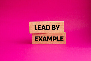 Lead by example message written on wooden blocks on pink background. Conceptual lead by example...
