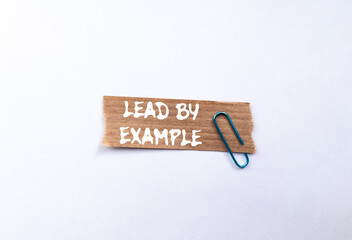Lead by example message written on ripped torn brown paper piece on white background. Conceptual...