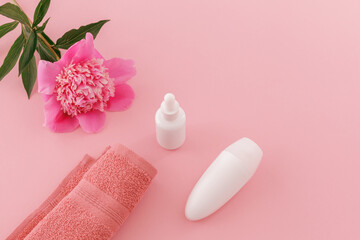 Towel with body care products and a peony flower on the pink background.